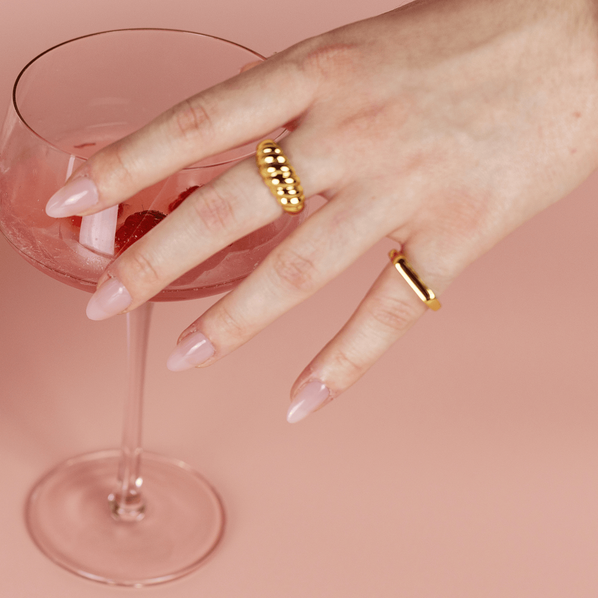 Limited Edition Pink Medium Almond Nails by CNVS Nails on a woman's hand that reaches for a cocktail 