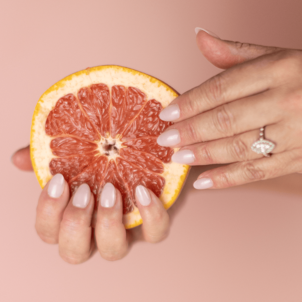 Limited Edition Pink Short Almond Nails by CNVS Nails modeled by a woman holding a sliced grapefruit.