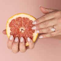 Limited Edition Pink Short Almond Nails by CNVS Nails modeled by a woman holding a sliced grapefruit.