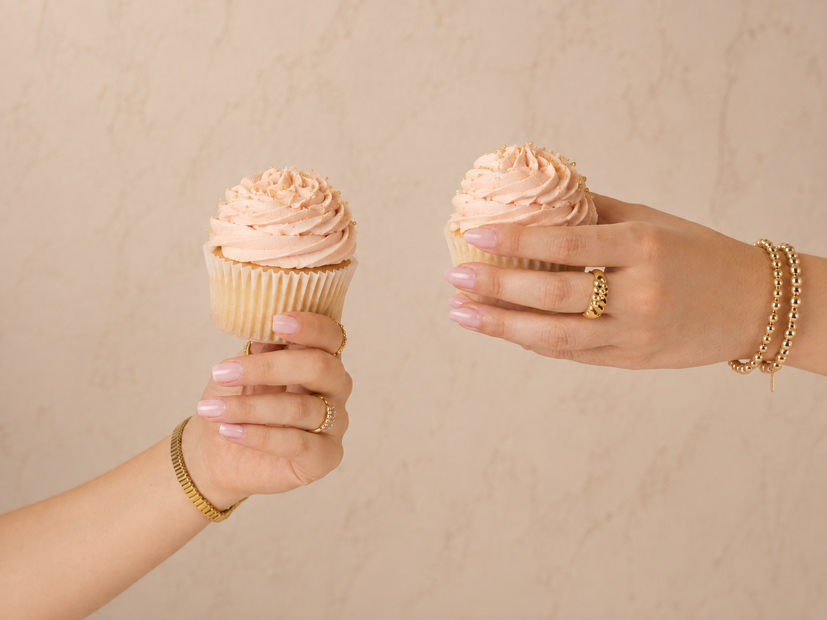 Two hands wearing glossy pink CNVS gel nail veneers and holding birthday cupcakes