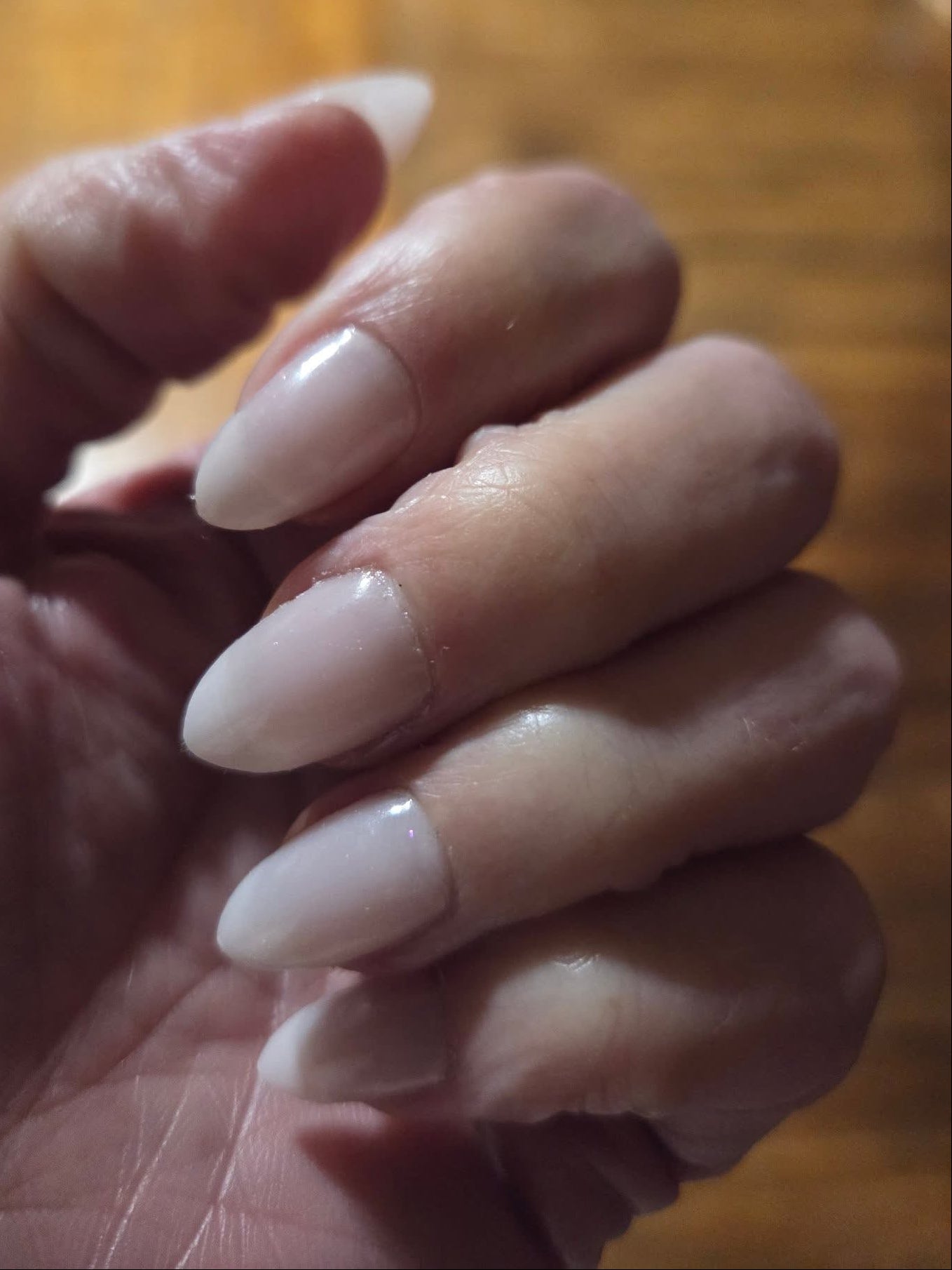 Close-up of a hand with light-colored nail polish on a wooden surface